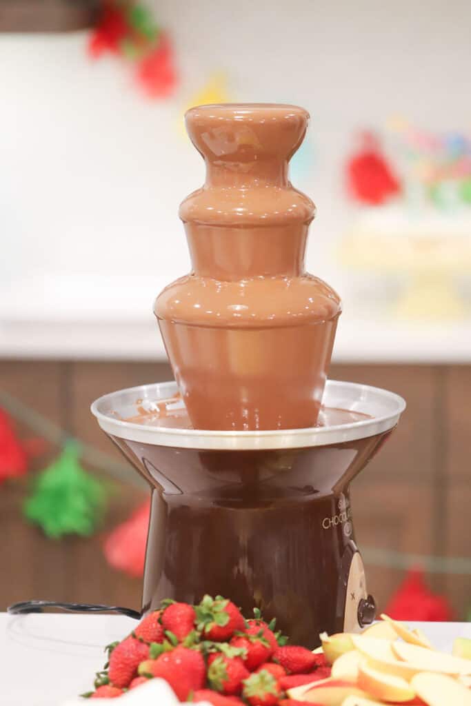 A chocolate fountain on a table surrounded by fresh fruit and other items for dipping.best chocolate for a Chocolate fountain, Chocolate fountain recipes. chocolate for fountain 