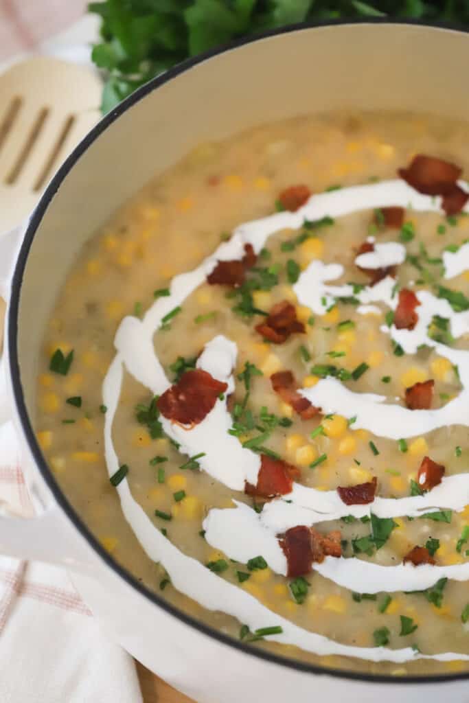 A dutch oven full of potato corn chowder and topped with creme fraiche, bacon bits, and parsley. An easy potato chowder soup