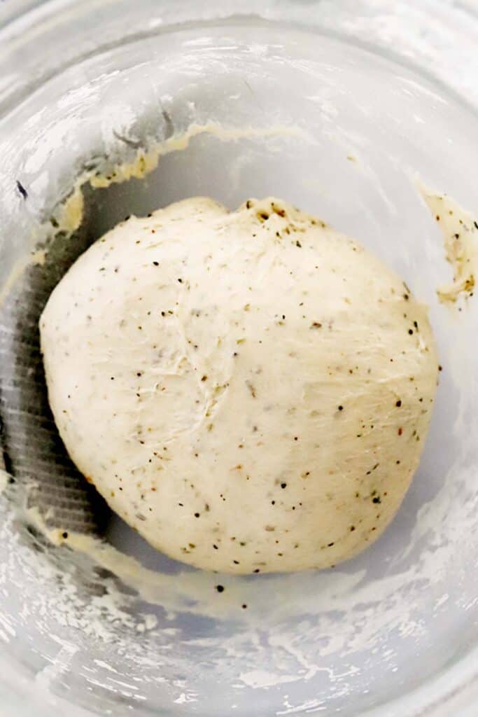 herbed focaccia bread dough in a mixing bowl. focaccia herbs in bread dough. Italian herb and cheese bread.