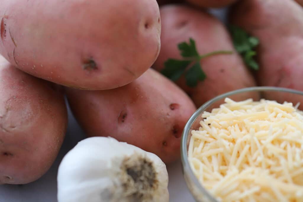 whole red potatoes, a whole head of garlic and a ramekin of shredded parmesan cheese to make garlic parmesan potatoes.