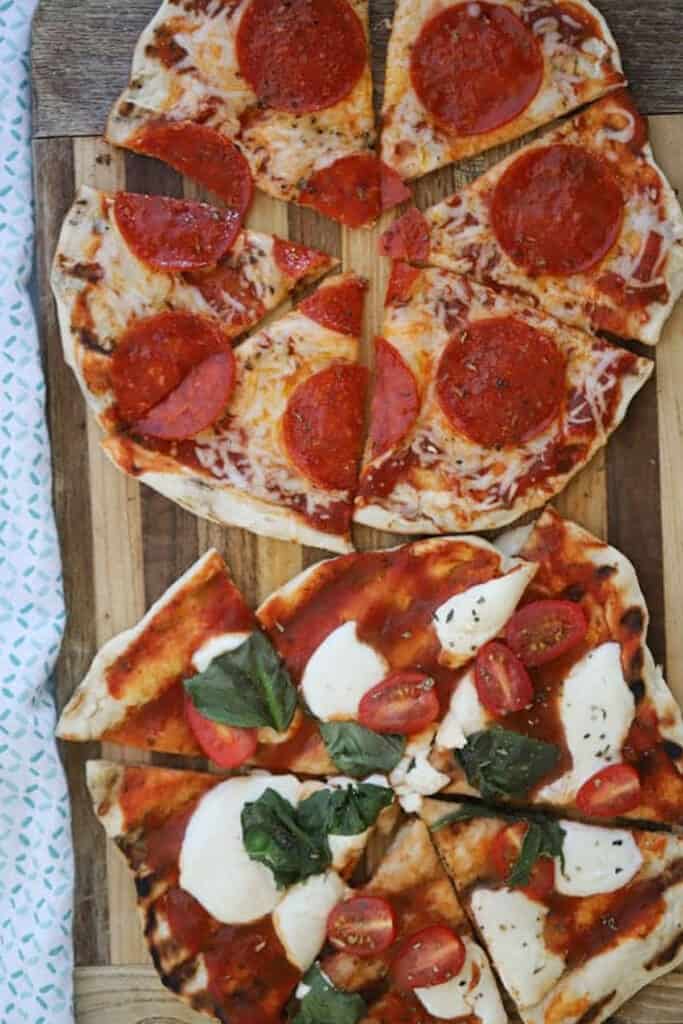 Grilled Pizza topped with cheese, pepperoni and fresh basil cut into slices on a cutting board. How to grill pizza.
