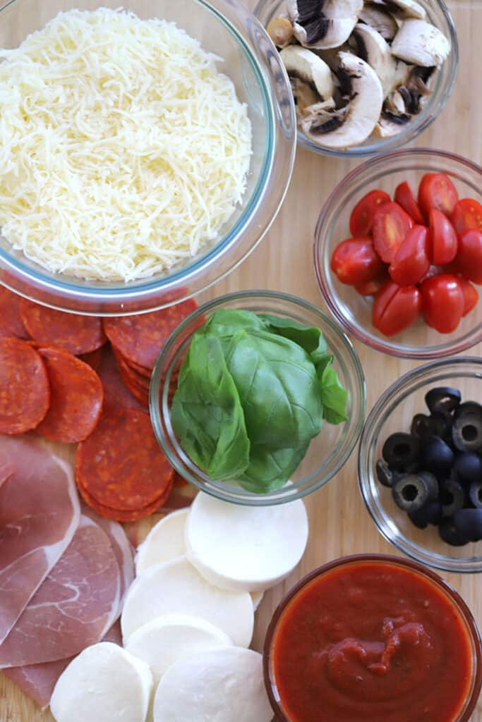 A top view of various pizza toppings in small glass ramekins. 