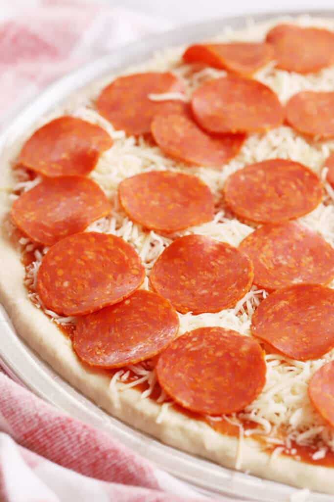 Pizza dough spread onto a pizza pan topped with sauce, cheese and pepperoni. how long to cook homemade pizza, temperature for pizza dough.