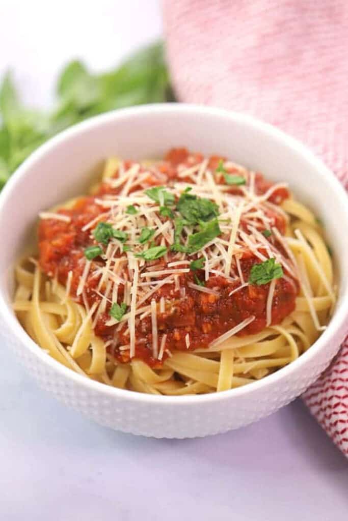 A white bowl full of fettuccini noodles topped with marinara sauce, Parmesan cheese and fresh basil. pasta with onions