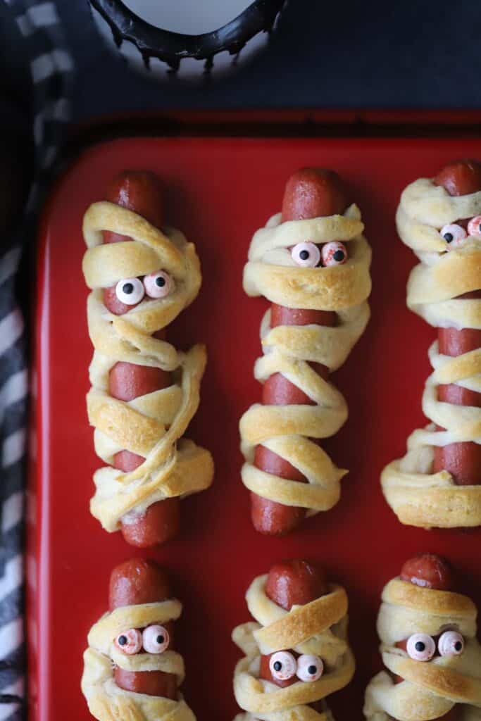Hotdog Mummy halloween food, these easy mummy hot dogs using crescent roll dough and tiny candy eyeballs.