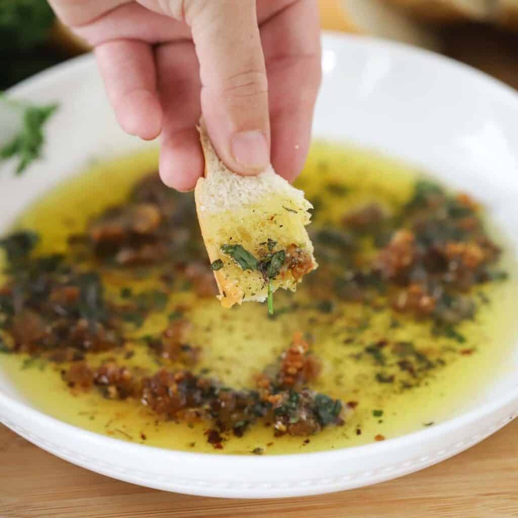 A hand dipping bread into olive oil dip.