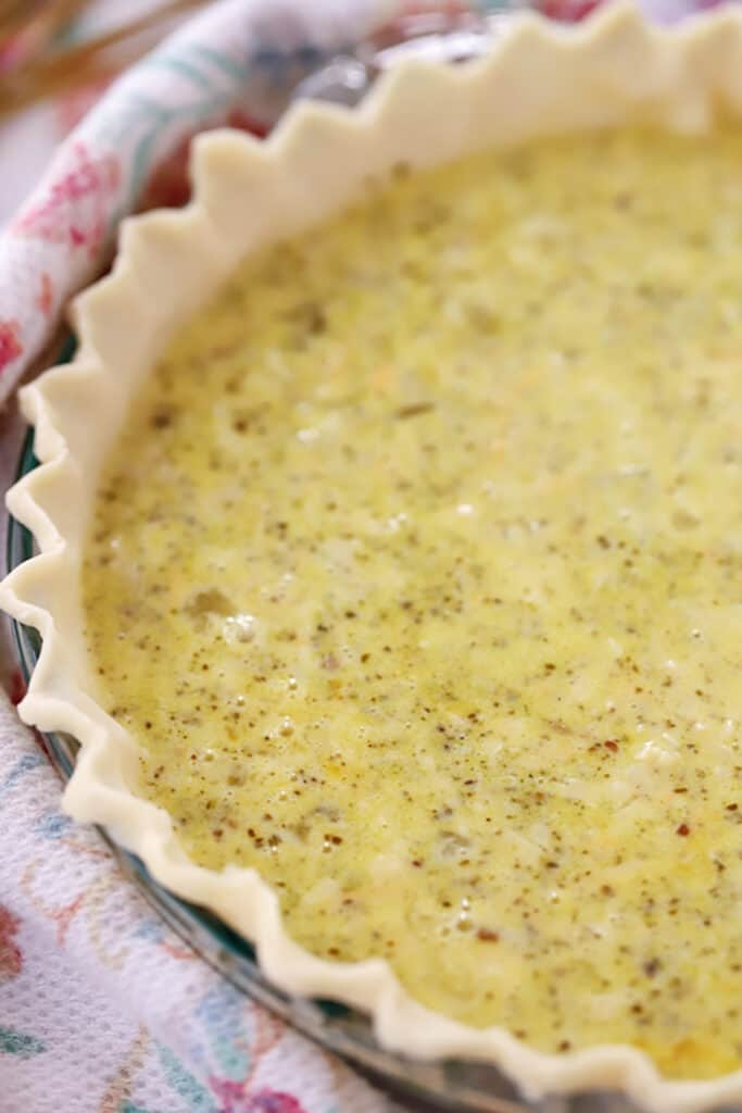 unbaked pesto quiche in a pie crust, ready to be baked, cheese in pesto. types of quiche. best quiche pesto recipe.