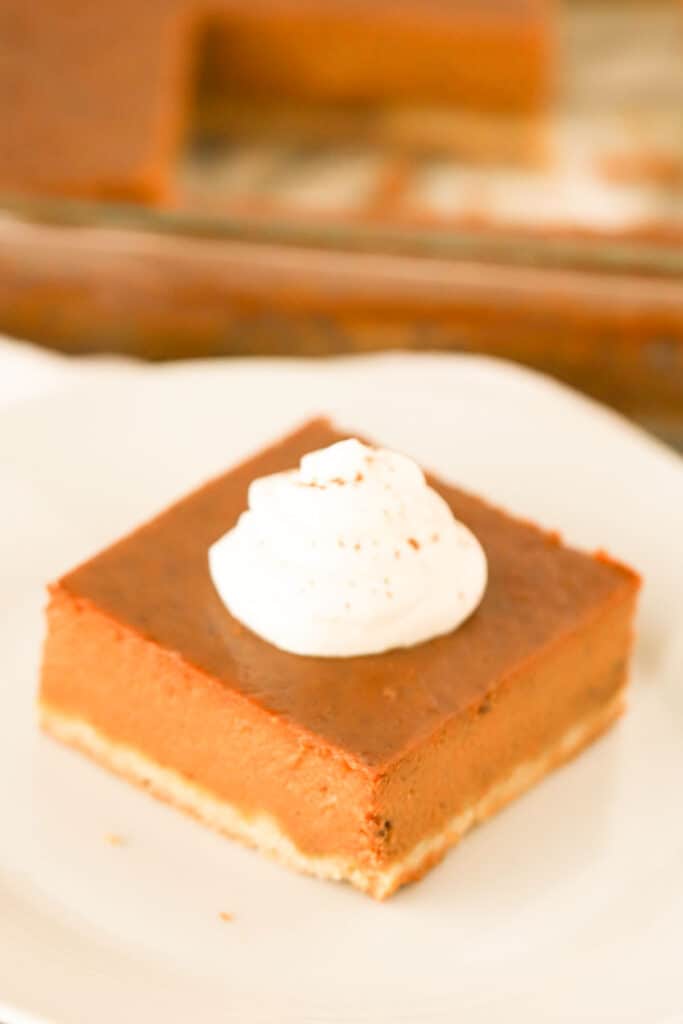 A pumpkin pie square on a white plate topped with whipped cream. Pumpkin pie bars recipe. Easy pumpkin pie bars.