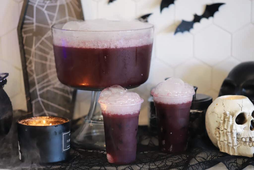 Halloween punch for kids in a large punch bowl with serving glasses. Dry ice helps to make this purple halloween punch extra spooky, perfect for Halloween parties.