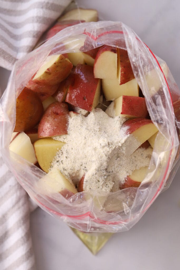 Quartered red potatoes in a ziplock bag topped with ranch seasoning mix. ingredients in a bag for recipe for ranch potatoes. roasted ranch potatoes. 