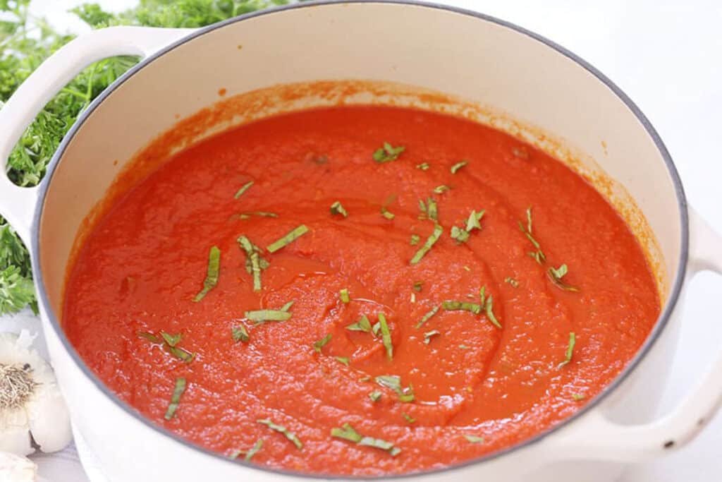 Homemade marinara sauce in a pot topped with fresh basil.