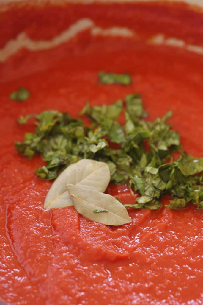Marinara sauce in a pot topped with fresh basil and bay leaves.