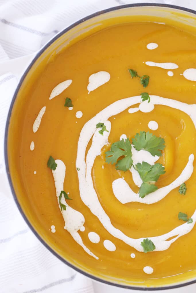 Roasted acorn squash soup in a bowl, garnished with sour cream and fresh cilantro. acorn butternut squash soup, roasted acorn squash soup, recipes for acorn squash soup.