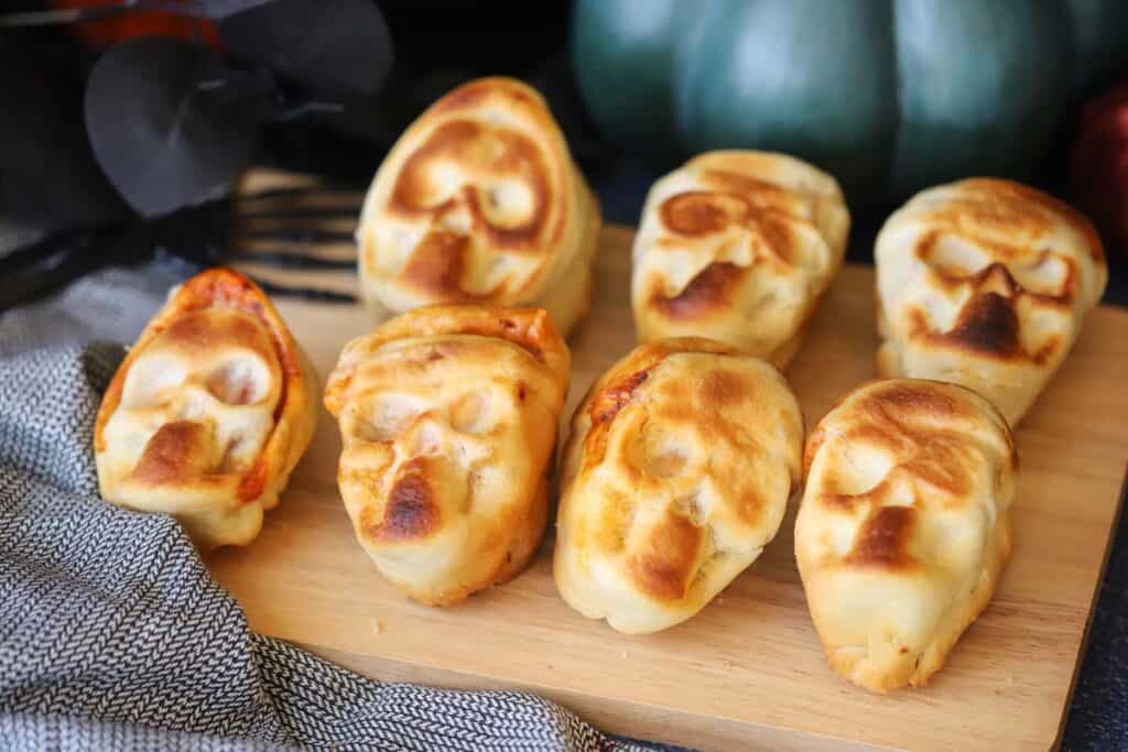 Best halloween pizza ideas include these pizza skulls, resting on a wooden cutting board.