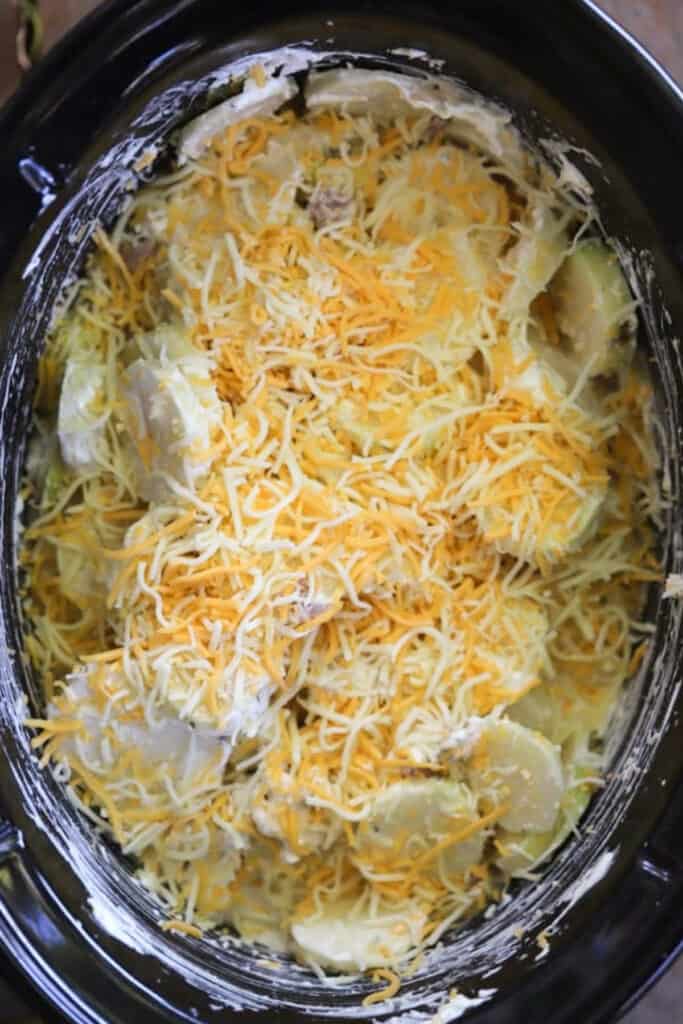 Scalloped Potatoes and Ham Slow Cooker recipe, topped with shredded cheese. Ham and potatoes in crock pot.