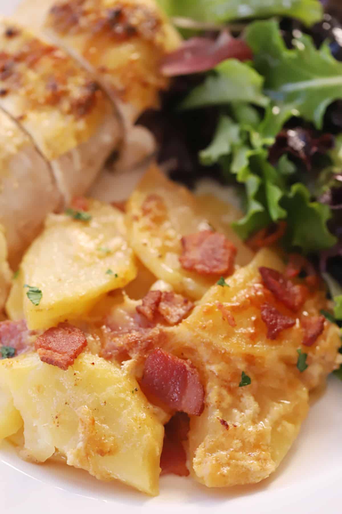 Smoky Bacon Potato Gratin 2 Scalloped potatoes with bacon and cheese on a serving plate with a side salad.