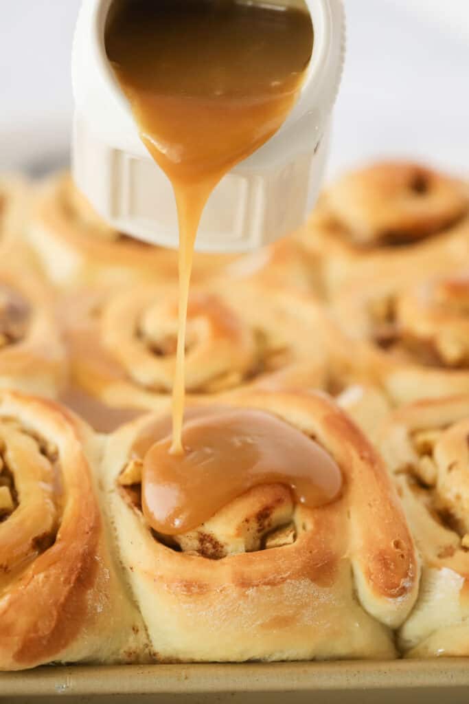 Caramel sauce being poured over apple caramel cinnamon rolls.