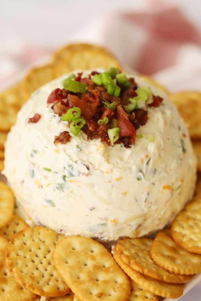 bacon cheddar cheese ball topped with bacon bits and sliced scallions, surrounded by Ritz crackers.