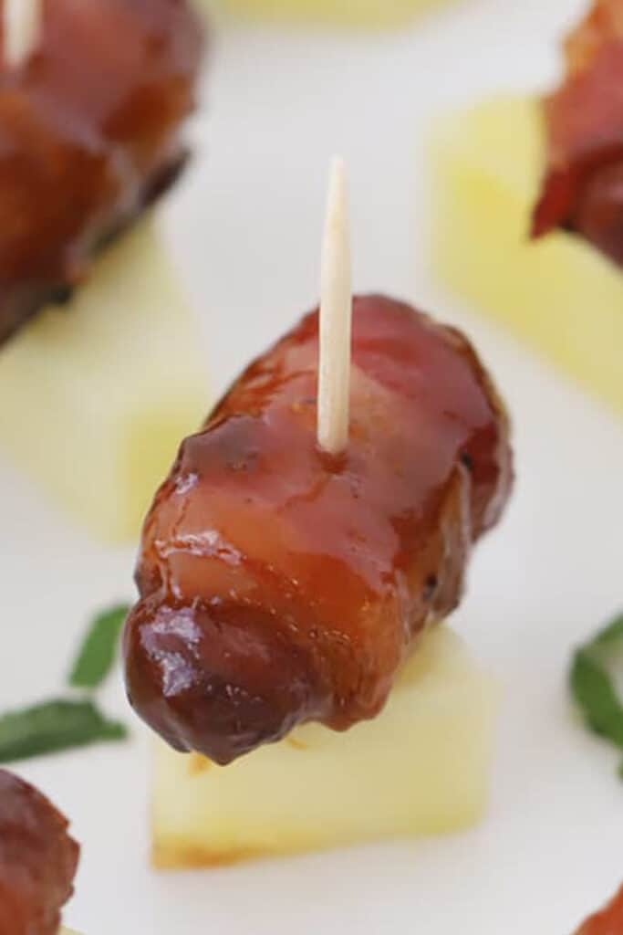 bacon wrapped smokies served on a piece of pineapple.