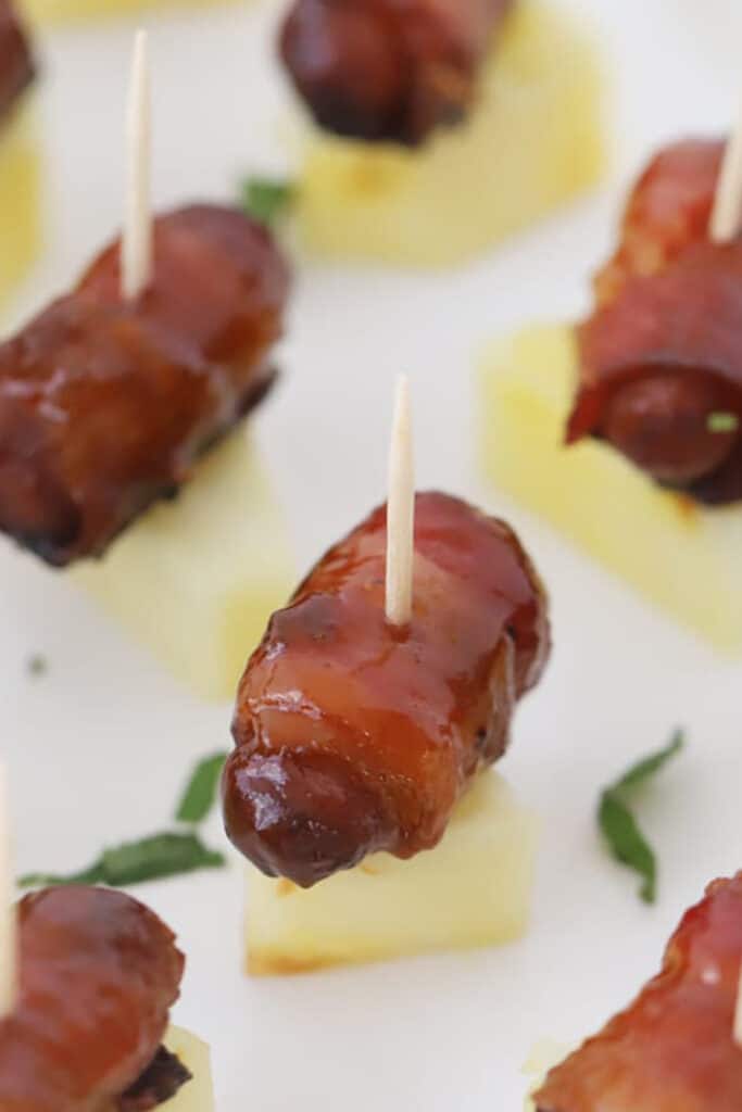 bacon wrapped smokies served on a piece of pineapple, bacon wrapped cocktail weenies.