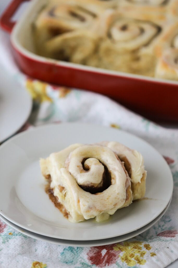 The best homemade cinnamon roll covered with cream cheese frosting on a white serving plate.