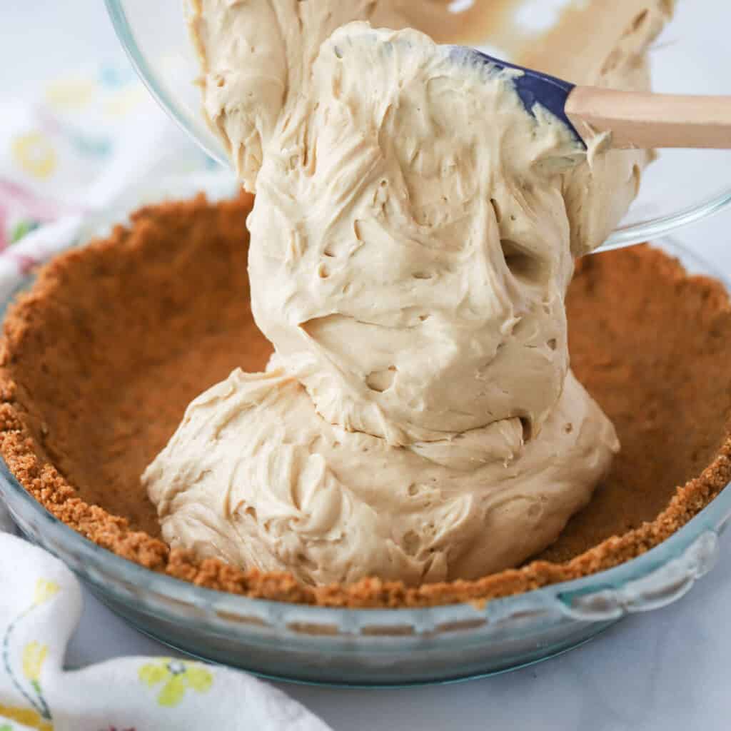 Cookie butter pie filling being added to a biscoff pie crust.