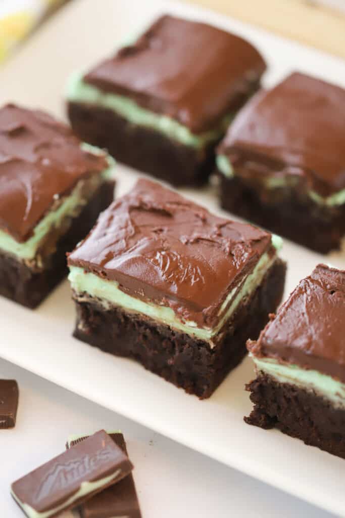 A serving plate full of Mint Chocolate brownies, with flavors of creme de menthe. There is a mint frosting layer and chocolate ganache layer on top.
