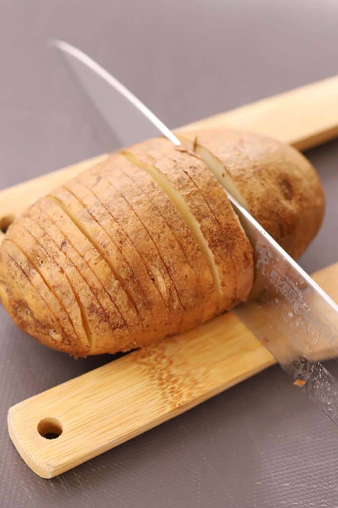 A knife thinly slicing through a potato using two wood spoons as guides