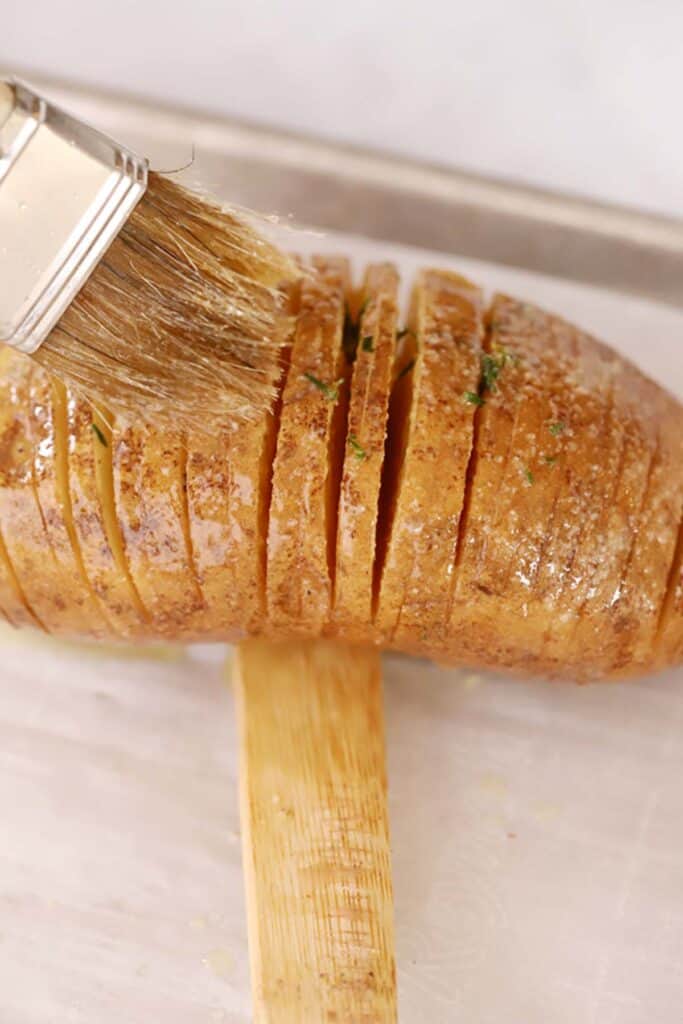Brushing melted butter and oil over the top of a Hasselback Potato, hasselback baked potatoes. 