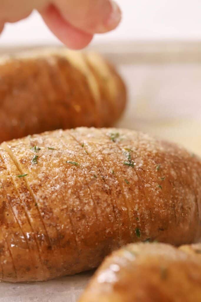 Fingers salting baked Hasselback Potatoes