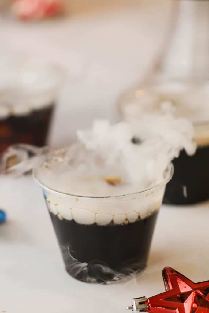 A cup full of homemade root beer that has a little smoke coming out from dry ice.
