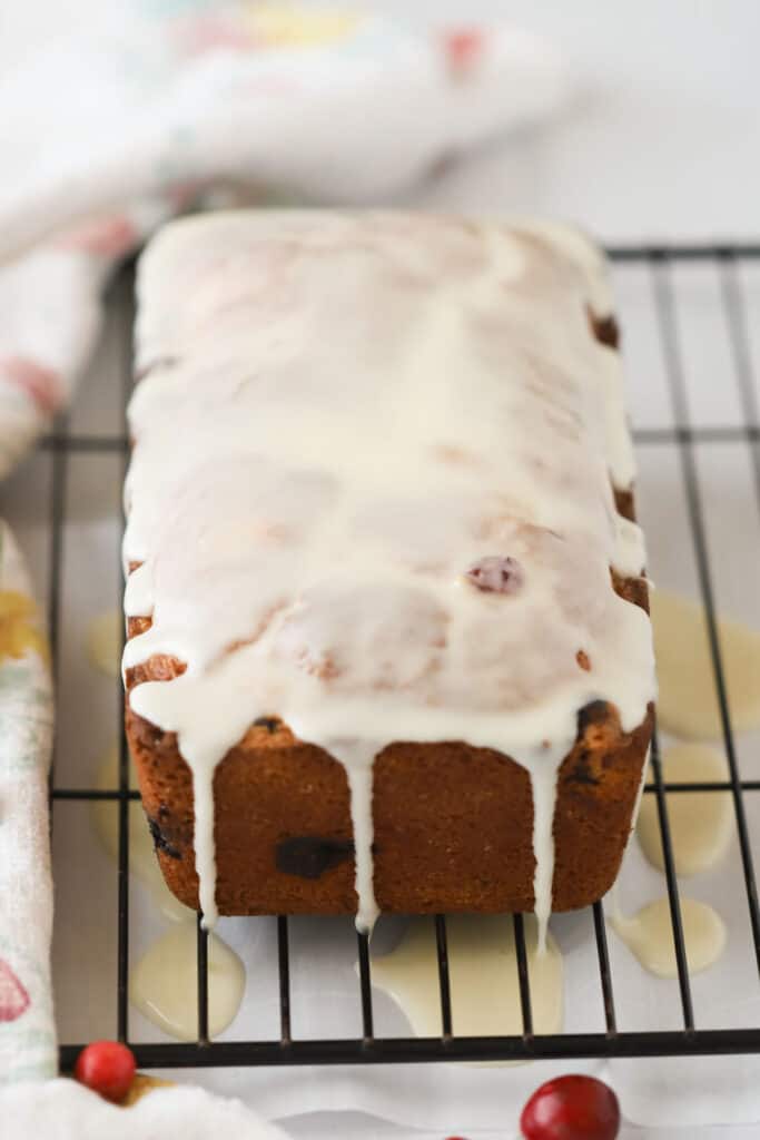 A loaf of cranberry cake recipe on a wire rack with glaze dripping over the top.