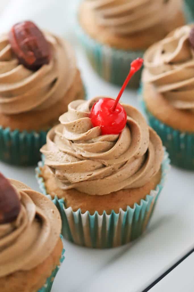 Root beer float cupcakes topped with root beer buttercream frosting and maraschino cherries.