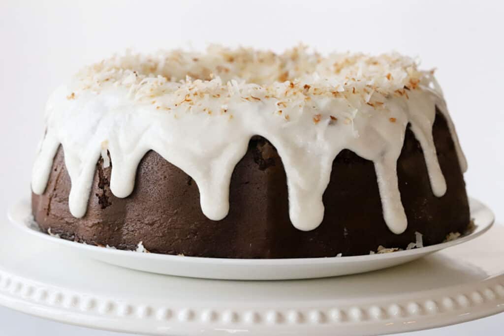 chocolate bundt cake with coconut filling on platter with almond glaze dripping down the sides.