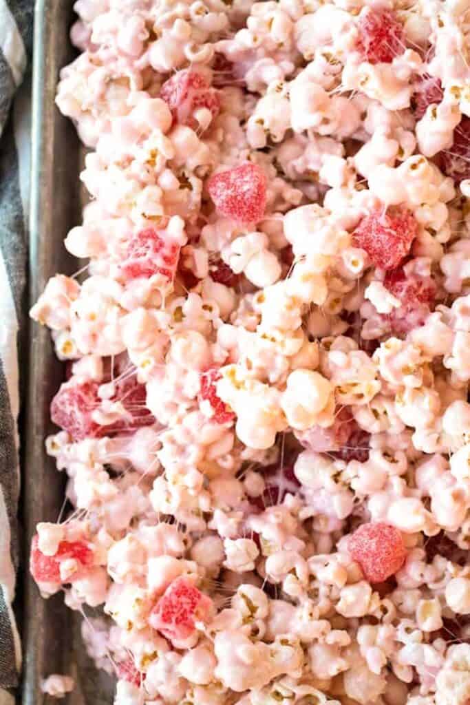 How to make cinnamon bear popcorn balls with marshmallows. A tray full of white chocolate drizzled popcorn mixed with gooey marshmallows and cinnamon bears.