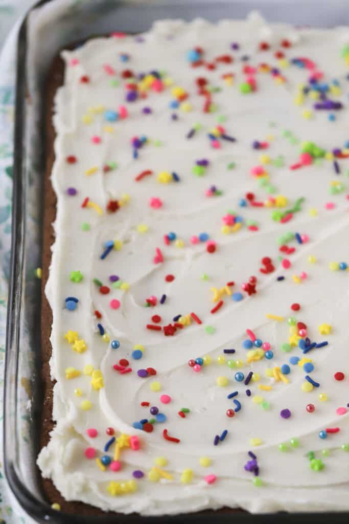 An easy Chocolate cookie bars recipe, the chocolate cookie dough is pressed into a baking sheet, baked, and then covered with white frosting and sprinkles.