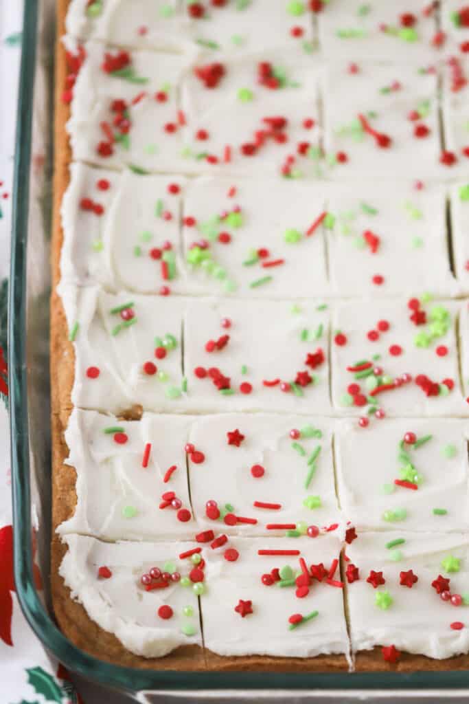 A tray of baked sugar cookie bars topped with buttercream frosting and festive sprinkles, easy christmas dessert bars that everyone loves.