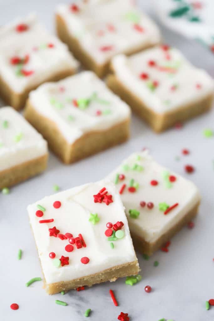 Rows of Christmas Sugar cookie Bars topped with christmas sprinkles and buttercream frosting. Easy sugar cookie Christmas bars.