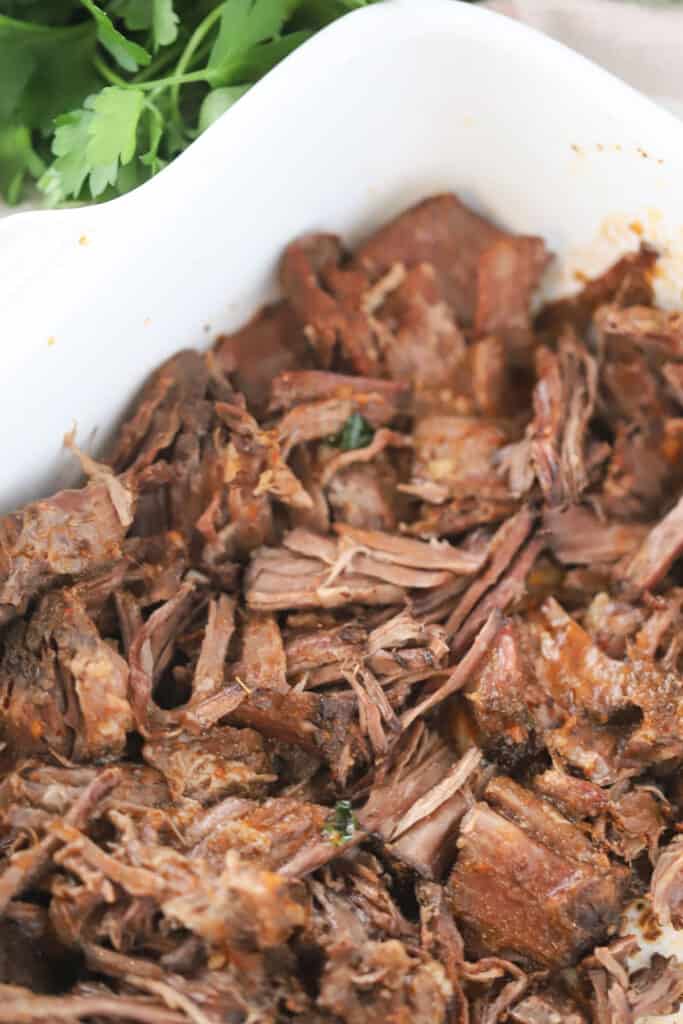 A white serving dish full of rich and savory beef birria made in a slow cooker. This is an easy shredded Mexican beef recipe.