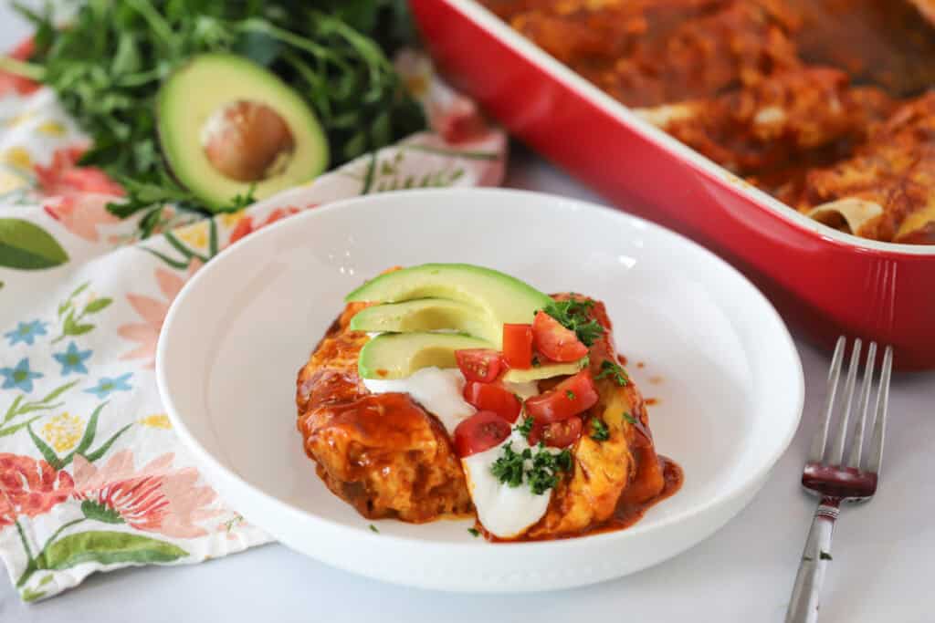 A white plate with a portion of Red Enchiladas, garnished with fresh cilantro. Enchilada recipe chicken red sauce.