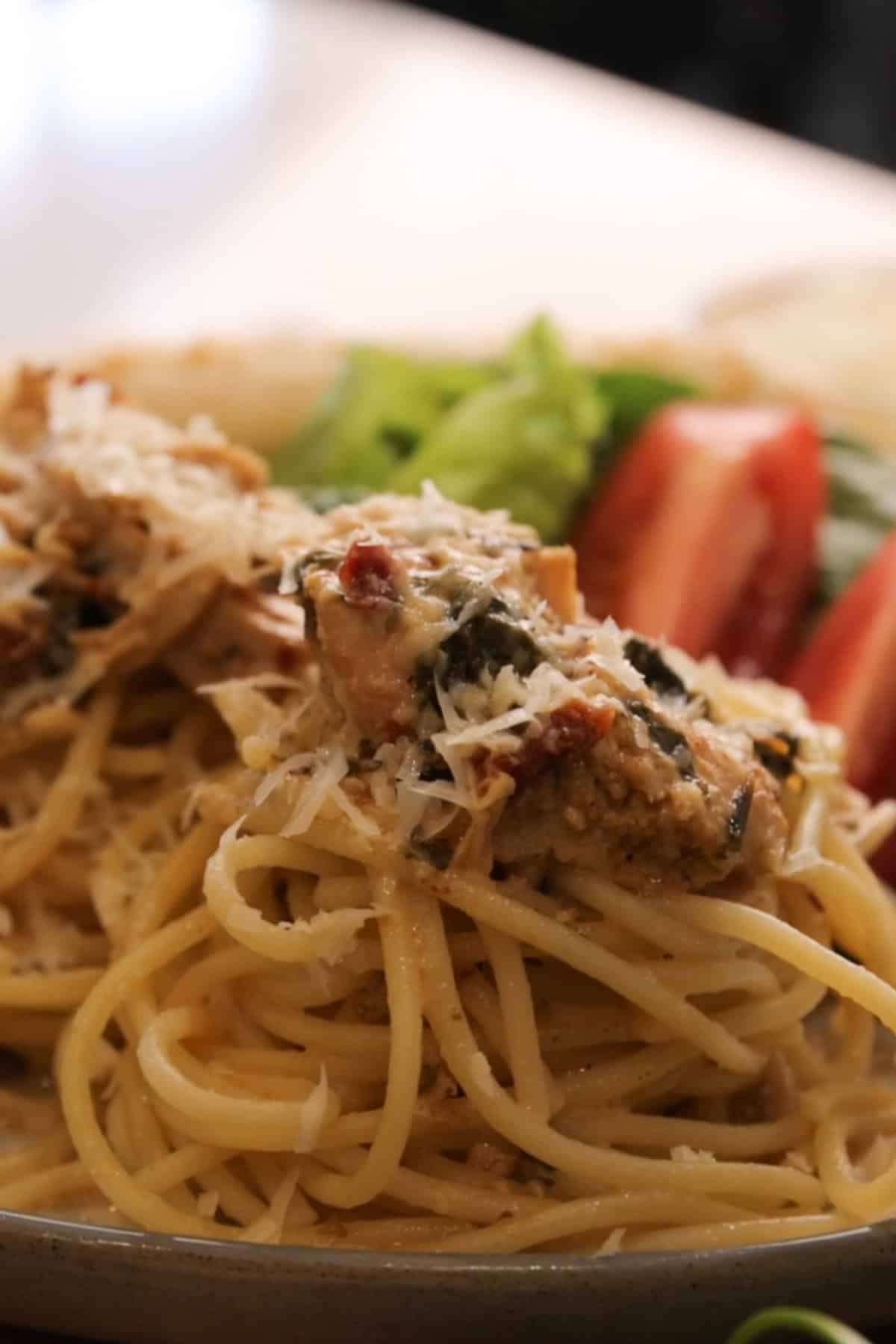 A dinner plate of spaghetti topped with Tuscan Chicken Crockpot Recipe.