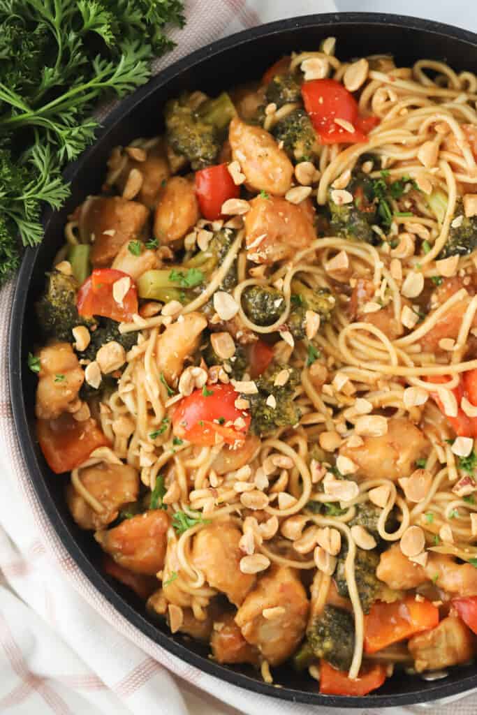 A skillet full of thai peanut sauce noodles with chicken and broccoli.