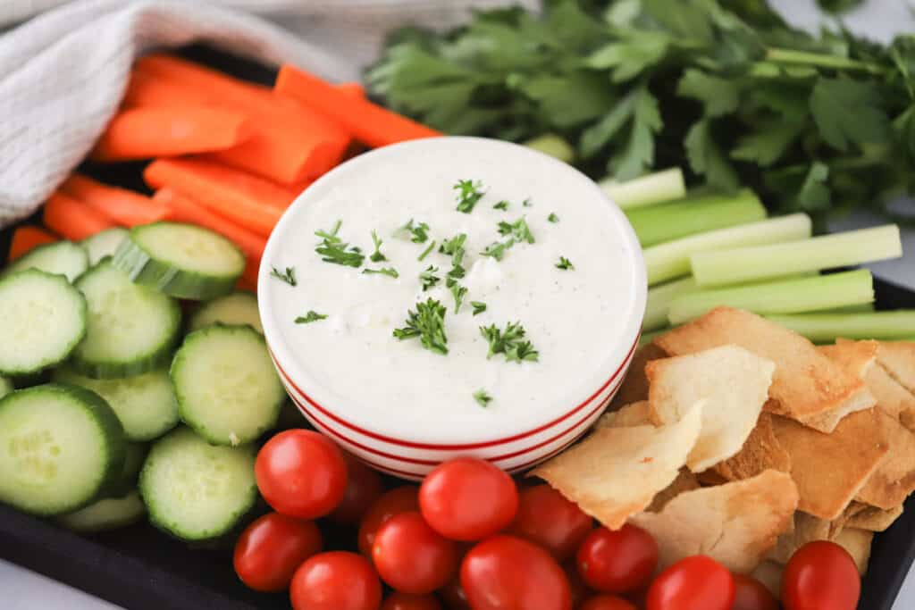 Easy Tzatziki recipe topped with fresh herbs and surrounded by fresh veggies and pita chips for dipping.