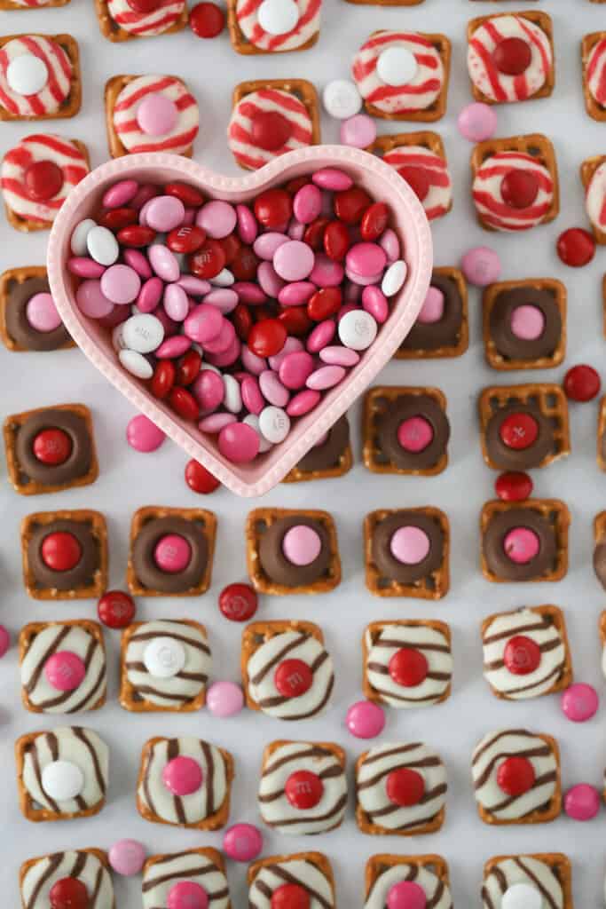 A tray full of Valentine's Day themed Hershey Kiss Pretzels bites made with M&Ms and small square pretzels.