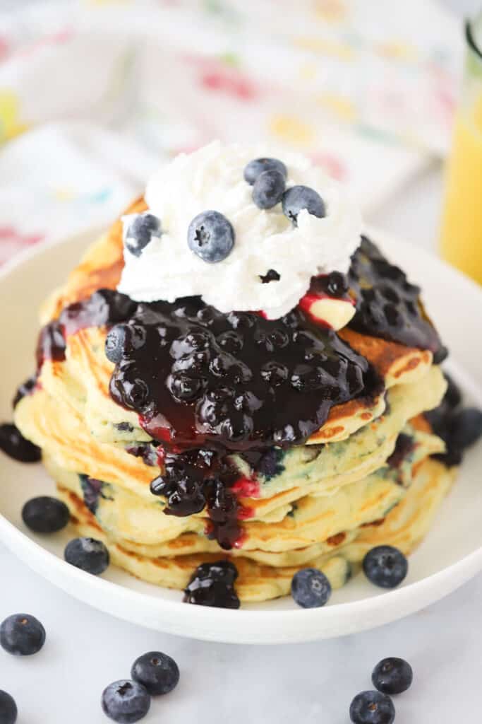 A stack of fluffy pancakes made using this lemon blueberry pancakes recipe topped, with blueberries and whipped cream. 