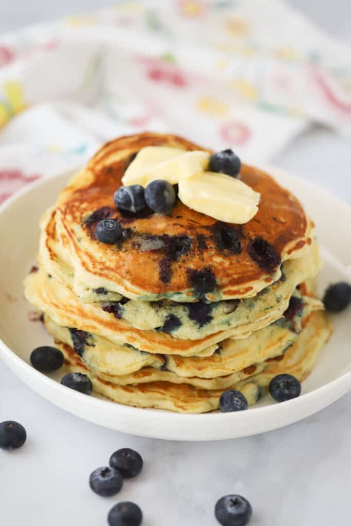 A stack of lemon blueberry pancakes topped with maple syrup and butter. Can be made into lemon ricotta blueberry pancakes, too.