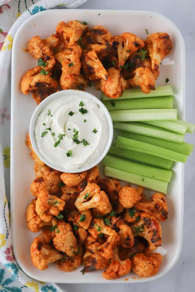 buffalo cauliflower bites on a serving platter with ranch dip and celery sticks.