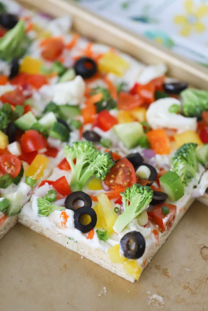 Crescent Roll Vegetable Pizza on a sheet tray topped with fresh veggies and olives, spread with ranch flavored cream cheese.