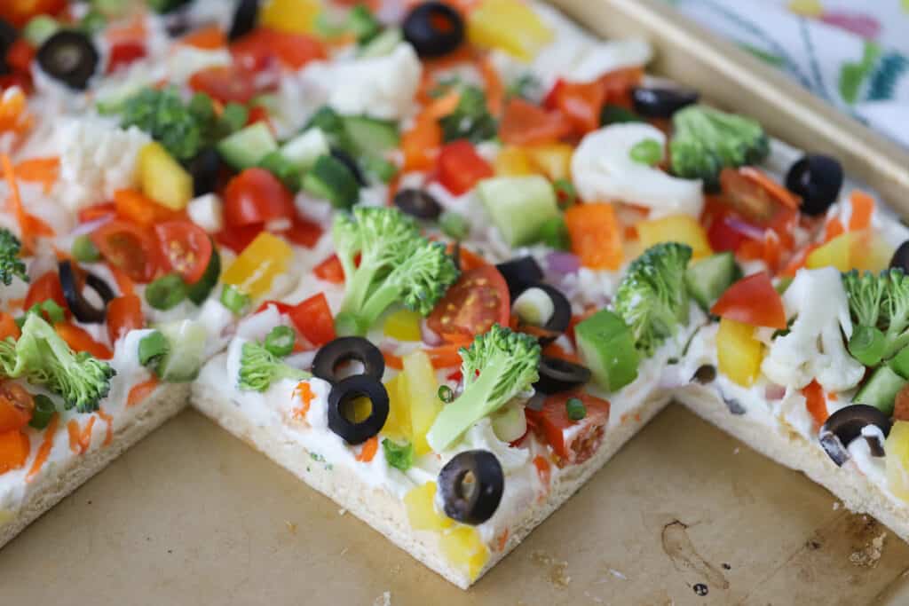 A sheet tray of crescent dough veggie pizza, topped with ranch cream cheese and veggies.