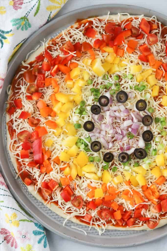 Homemade vegetable pizza made into a rainbow veggie pizza with colorful vegetables on top.